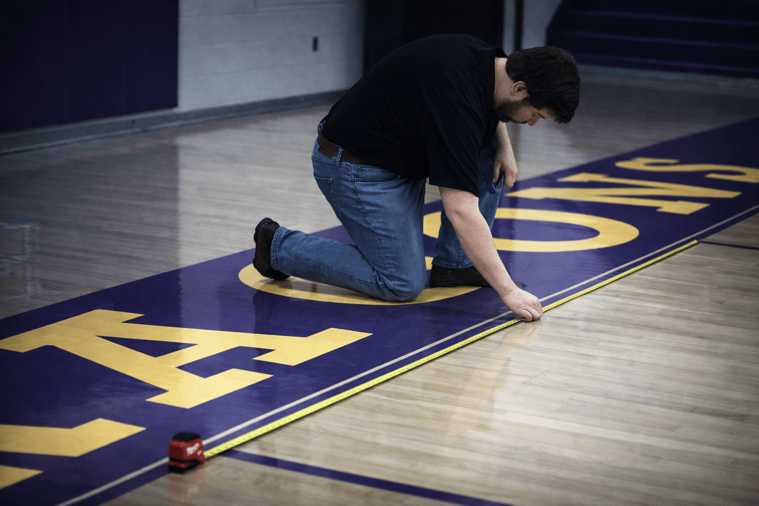 Luxedo technician measuring and taping a basketball court floor before projection mapping installation